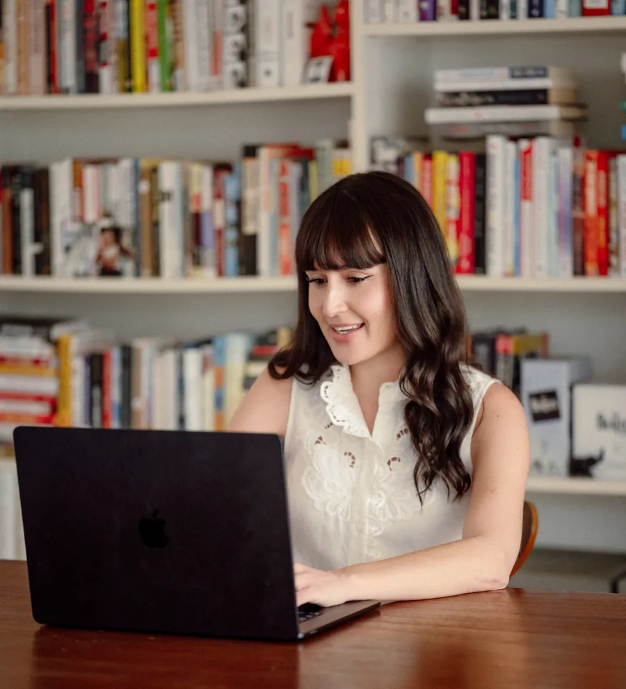 Dr. Ileana Hernandez smiling at her laptop in front of a full bookshelf